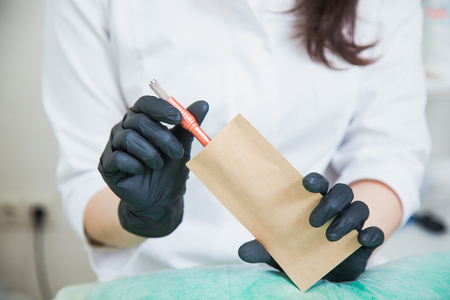 Cosmetologist put tatoo pen into sterilizing craft package. Beautician prepares equipmentの写真素材