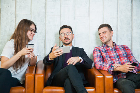 Group of three young people hold smartphones talk and smile. Internet online sms chat social net