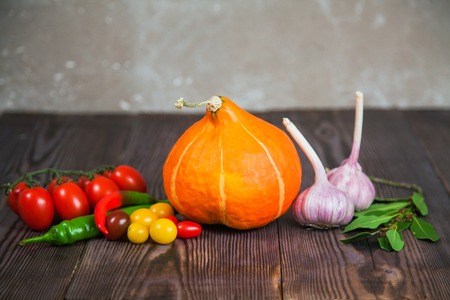 Pumpkin tomatoes garlic cili peppers on wooden table. harvest raw eating healthy diet background composition copy spaceの写真素材