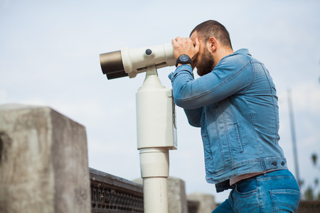 Trendy male person look in binocular telescope. Young man in jeans wear casual denim jacket. Urban lifestyleの写真素材