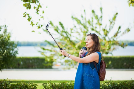 Young woman with smoothie selfie stick photo herself outdoors. trendy girl have fun with her smartphoneの写真素材
