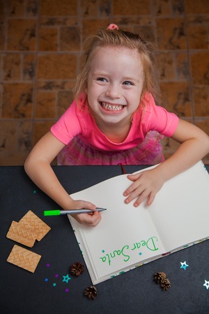 Little child writing letter to Santa Claus on a blank sheet of paper. Small hands of a girl holding marker. Christmas preparation concept.の写真素材