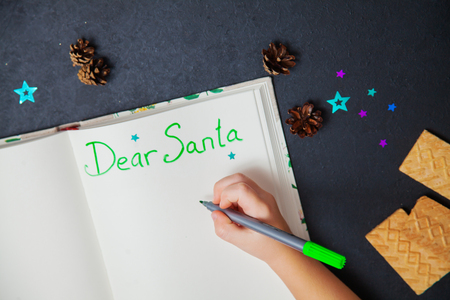 Little child writing letter to Santa Claus on a blank sheet of paper. Small hands of a girl holding marker. Christmas preparation concept.の写真素材