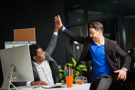 Two businessmen celebrate victory, goal reach, high five. Hardworking male workers. Hipster students at light office room with computer monitor. Satisfied with job doneの写真素材