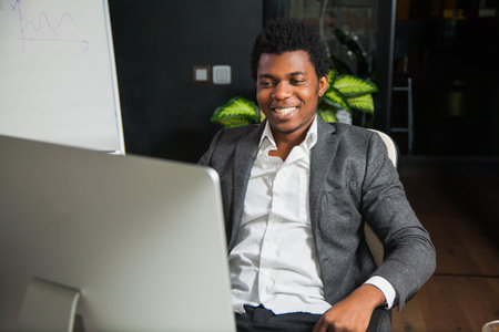 Hardworking smiling afroamerican at office look at computer monitor. Young handsome black man...