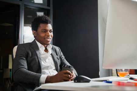 Hardworking smiling afroamerican at office look at computer monitor. Young handsome black man...