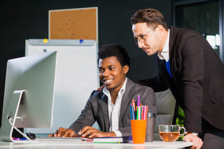 Two businessmen looking at computer screen, teamwork concept. Male caucasian and african guys work...