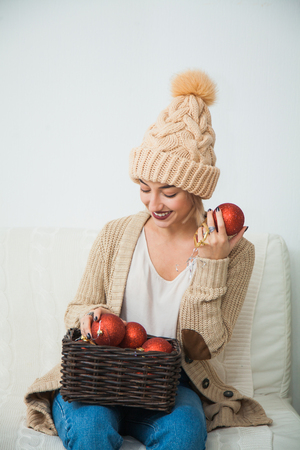 Young girl in cozy knitted clothes hold christmas balls decoration basket. New year x-mas concept. Warm wool hat indoors.の写真素材