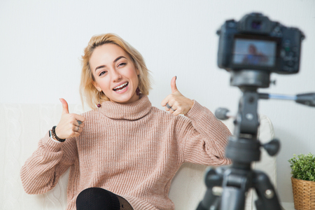 Blogging concept. Young female vlogger next to video camera at home. Beautiful woman recording vlog message at home for her internet channelの写真素材