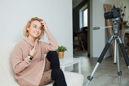 Blogging concept. Young female vlogger next to video camera at home. Beautiful woman recording vlog message at home for her internet channelの写真素材