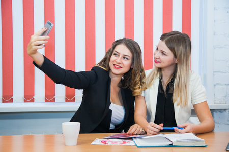 Two girlfriends sit together talk discuss smile make selfie. Young women meet at working place for freelancers.の写真素材