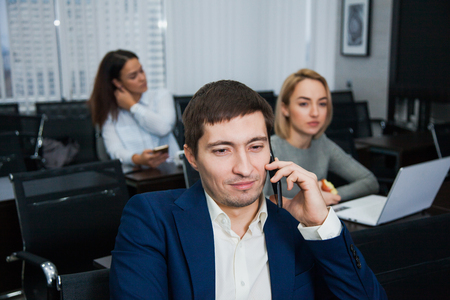 Young confident businessman talking by phone at office. Two women on background, Teamwork, brainstorming, business situation conceptの写真素材