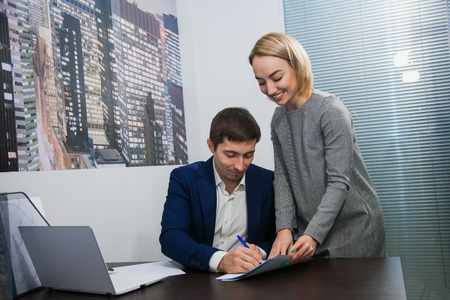 Female personal assistant gives papers for sign to boss businessman. Business routine at officeの写真素材