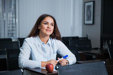 Female student in empty classroom sit and listen carefully. Young curly woman at office table in auditoriumの写真素材