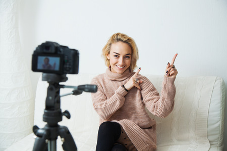Blogging concept. Young female vlogger next to video camera at home. Beautiful woman recording vlog message at home for her internet channelの写真素材