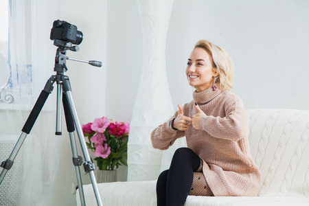 Blogging concept. Young female vlogger next to video camera at home. Beautiful woman recording vlog message at home for her internet channelの写真素材