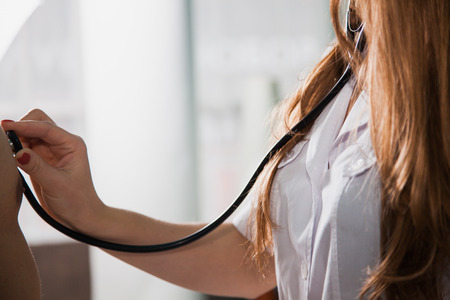 Female doctoc examining patient with stethoscope at medical cabinet an clinic. Health care and physician conceptの写真素材