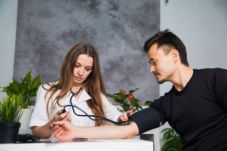 Female doctor measuring arterial blood pressure for patient on tonometer at clinic. Health care and physician conceptの写真素材