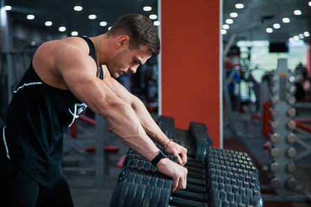 Fit male athlete getting ready for dumbbell workout. Handsome man at fitness gym take rest and breathe. Fitness, bodycare and active lifestyle concept.の写真素材