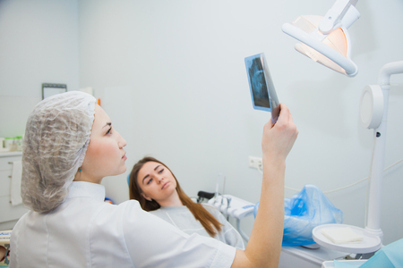 Female doctor dentist examining x-ray of human jaw. Professional stomatologist showing dental x-ray image to patient at clinic office.の写真素材