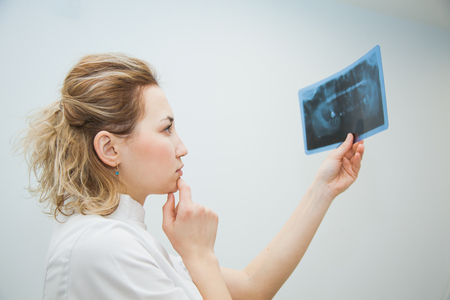 Female doctor dentist examining x-ray of human jaw. Professional stomatologist checking dental x-ray image at clinic office.の写真素材