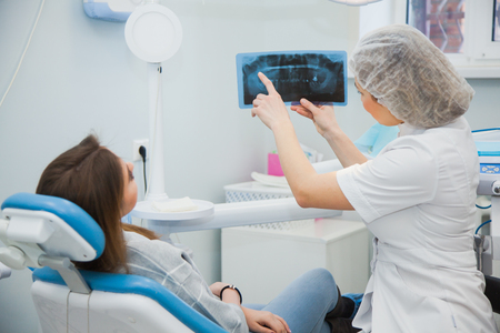 Female doctor dentist examining x-ray of human jaw. Professional stomatologist showing dental x-ray image to patient at clinic office.の写真素材