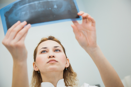 Female doctor dentist examining x-ray of human jaw. Professional stomatologist checking dental x-ray image at clinic office.の写真素材