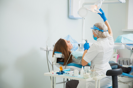 Female stomatologist in blue protective mask examining patient's teeth. Dentist caries treatment at dental clinic office. People, medicine, stomatology and health care conceptの写真素材