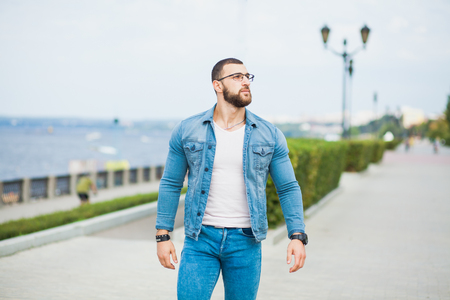 Handsome athletic fit man in jeans wear fitness model outdoors copy space. Young male with perfect muscular body poses to cameraの写真素材