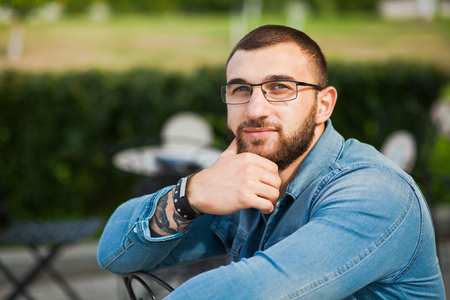 Confident young man in a street cafe. Handsome guy in jeans clothes, stylish male person, trendy look, hipster beard, copy spaceの写真素材