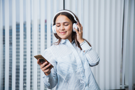 Young business woman listen to music on her leisure time at work. Attractive female manager at office with headphones and smartphone at her workspaceの写真素材