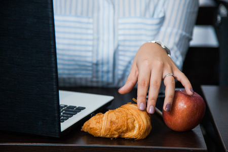 Eating at work, compulsive eating, tea time coffee break at office. Female businesswoman eat croissant and apple with big mug of hot drink.の写真素材