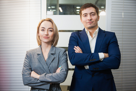 Two respectable business people in formal suits stand together. Man and woman at office room pose to camera. Teamwork, cooperation, success conceptの写真素材