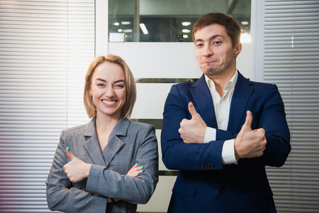 Two respectable business people in formal suits stand together. Man and woman at office room pose to camera. Teamwork, cooperation, success conceptの写真素材