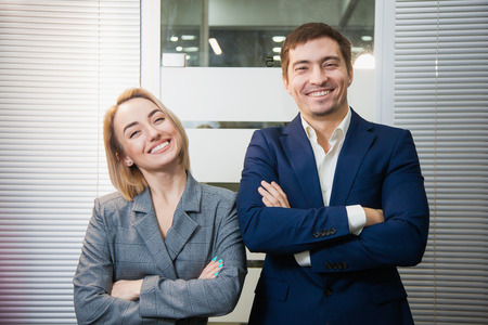 Two respectable business people in formal suits stand together. Man and woman at office room pose to camera. Teamwork, cooperation, success conceptの写真素材