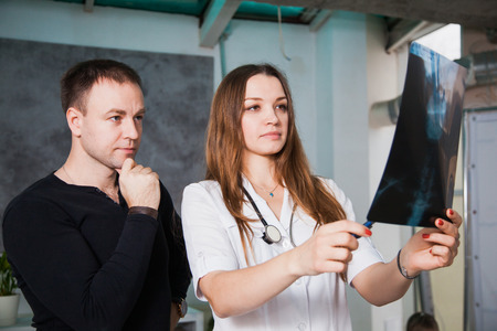 Doctor and patient examine head roentgen at clinic. Young professional female doctor showing x-ray of human scull during patients visit. Health medicine diagnostics conceptの写真素材