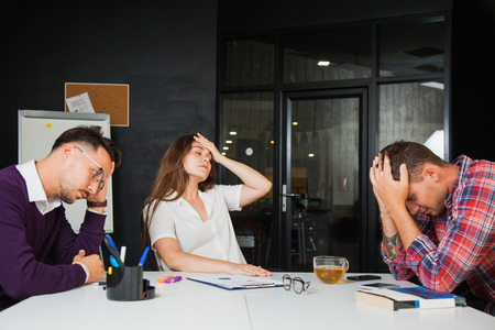 Three young businessmen have headache at office, sad failure. Disappointed people at workの写真素材