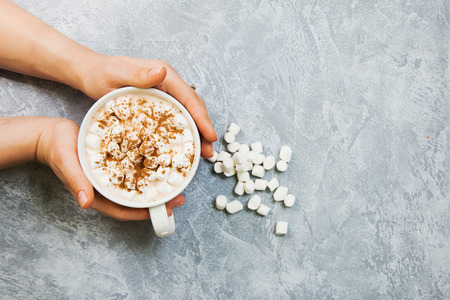 female hands hold big mug with cacao and marshmallow on gray background. Copy spaceの写真素材
