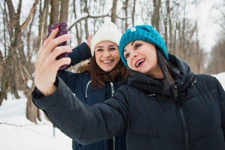 Two women friends outdoors in knitted hats on a snowy cold winter weather. Smiling girls in warm...