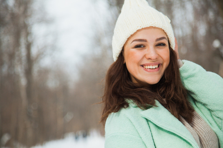 Young pretty woman with happy smile n white hand-knitted hat. Winter snowy day, frosty weather, copy space.の写真素材