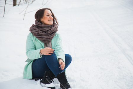 Young pretty lady in warm clothes sit on white snow on a winter day. Copy spaceの写真素材