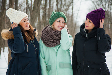 Three women friends outdoors in knitted hats on a snowy cold winter weather. Smiling girls in warm clothes.の写真素材