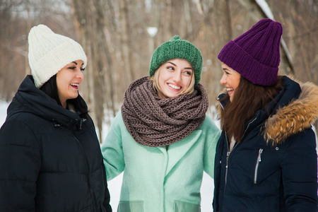 Three women friends outdoors in knitted hats on a snowy cold winter weather. Smiling girls in warm clothes. Closeupの写真素材