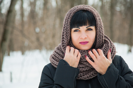 Pretty dark haired lady in warm cozy snood. Winter snowy day, frosty weather, copy space.の写真素材