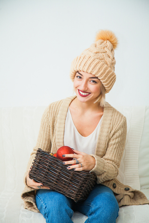 Young girl in cozy knitted clothes hold christmas balls decoration basket. New year x-mas concept. Warm wool hat indoors.の写真素材