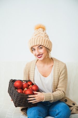 Young girl in cozy knitted clothes hold christmas balls decoration basket. New year x-mas concept. Warm wool hat indoors.の写真素材