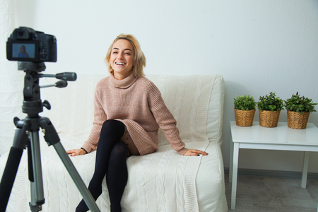 Creative young woman recording video blog for social media network. Blogging concept. Young female vlogger next to video camera at home, vlog message for internet channelの写真素材