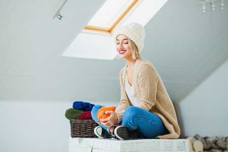 Young woman in warm hand knitted hat at home. beautiful lady indoors with pumpkin in hands, smiling happily. Autumn harvest hygge conceptの写真素材