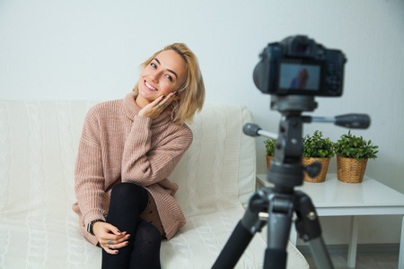 Creative young woman recording video blog for social media network. Blogging concept. Young female vlogger next to video camera at home, vlog message for internet channelの写真素材