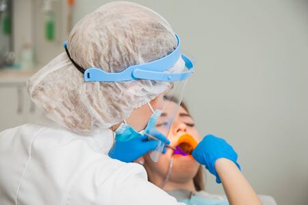 Female dentist work with light-curing seal, patient with caries on chair. Stomatologist and patient at clinical office. Toothcare conceptの写真素材